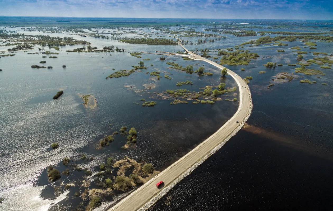 Затопленная дорога среди воды с автомобилем.